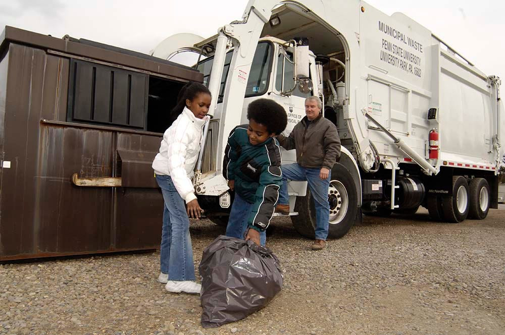 kids with a trash bag in front of a garbage truck