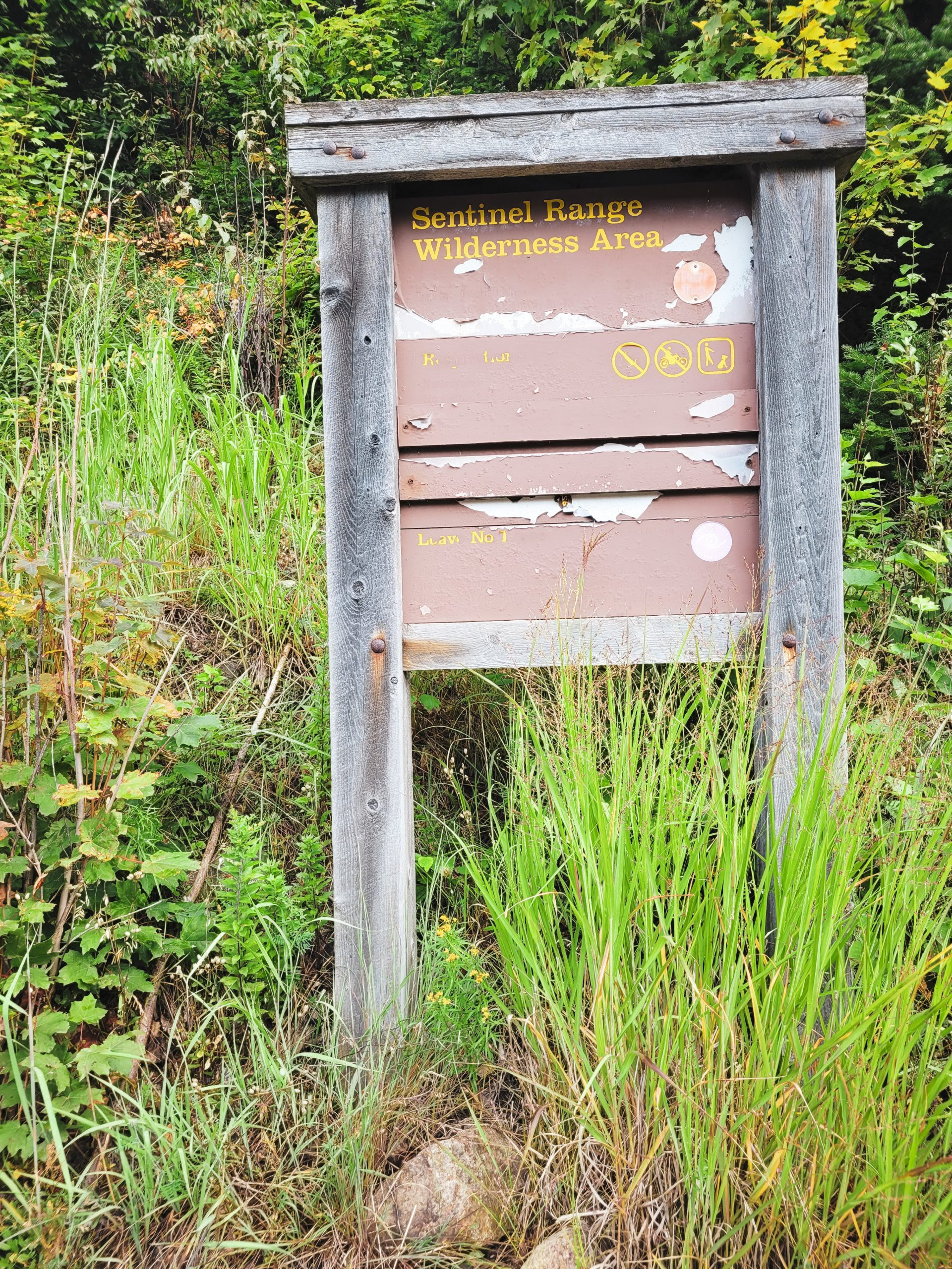 A barely legible trailhead sign marks the entrance to the Pitchoff Mountain and Balanced Rocks trails in the Adirondacks.