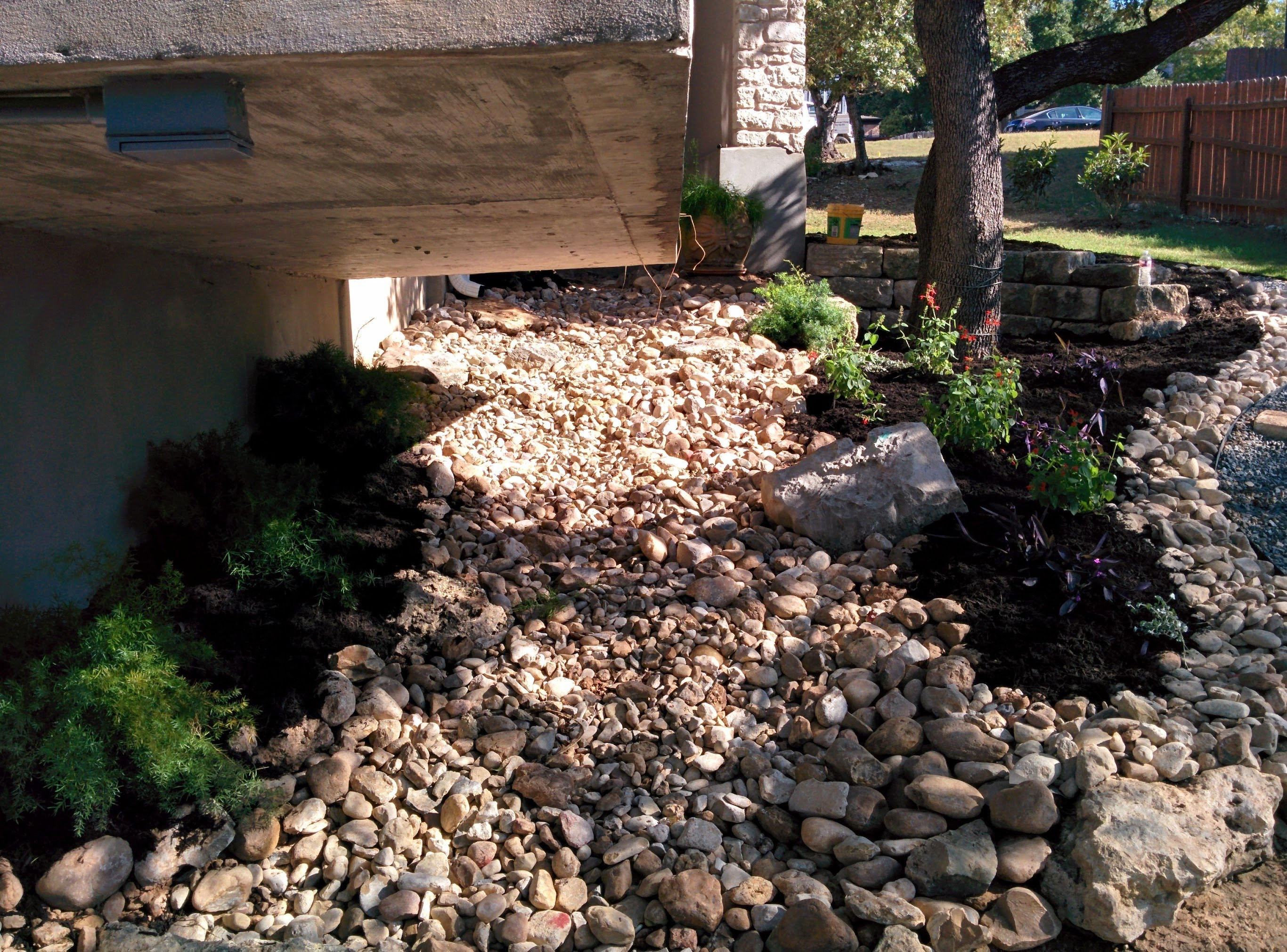 Dry creek bed landscape design, demonstrating the use of rocks for drainage and visual interest in a sloped garden.