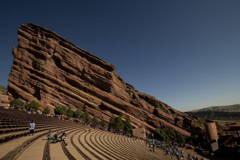 Widespread Panic concert at Red Rocks Amphitheatre, showcasing the stage illuminated with colorful lights and the silhouettes of Ship Rock and Creation Rock monoliths framing the performance.