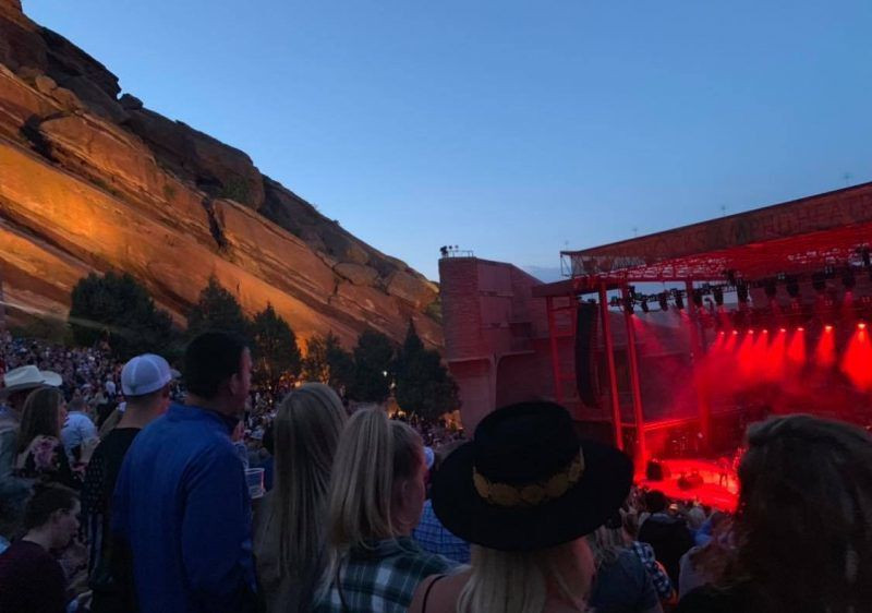 Night view of Red Rocks Amphitheatre during a concert, with stage lights and ambient lighting creating a warm glow against the dark red rock formations.