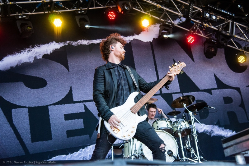 Sam Bettley and James Cassells of Asking Alexandria performing at Blue Ridge Rock Festival Day 2. The bassist and drummer are playing together energetically on stage.