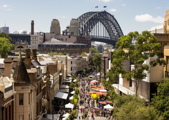 Weekend markets bustle in The Rocks, Sydney, with the Harbour Bridge providing a majestic backdrop to the stalls and shoppers.