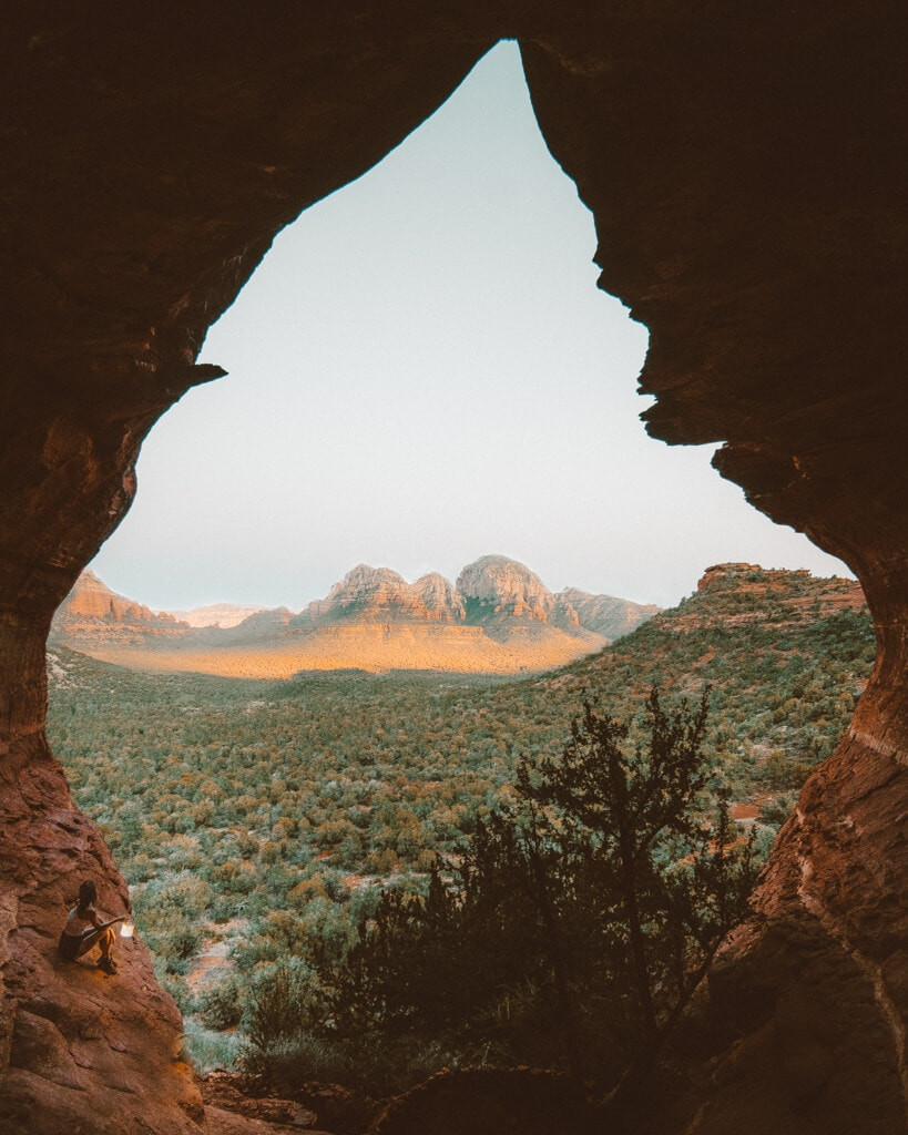 A female hiker enjoys the serene sunrise from Birthing Cave in Sedona, Arizona, taking in the panoramic views.