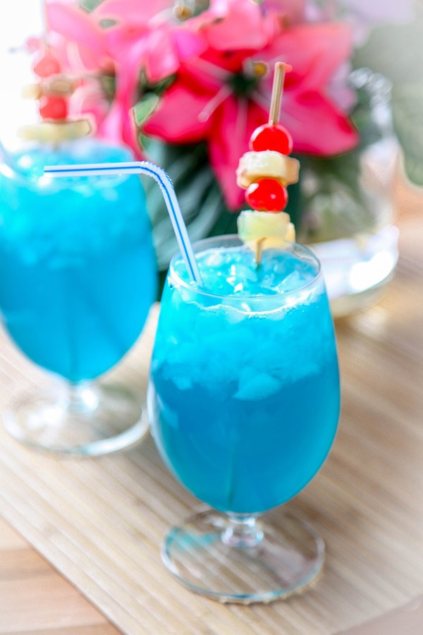 2 blue rum cocktails on a bamboo placement with a tropical flower in the background.