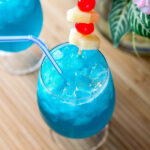 a closeup of a blue Hawaii cocktail garnished with pineapple and maraschino cherries.