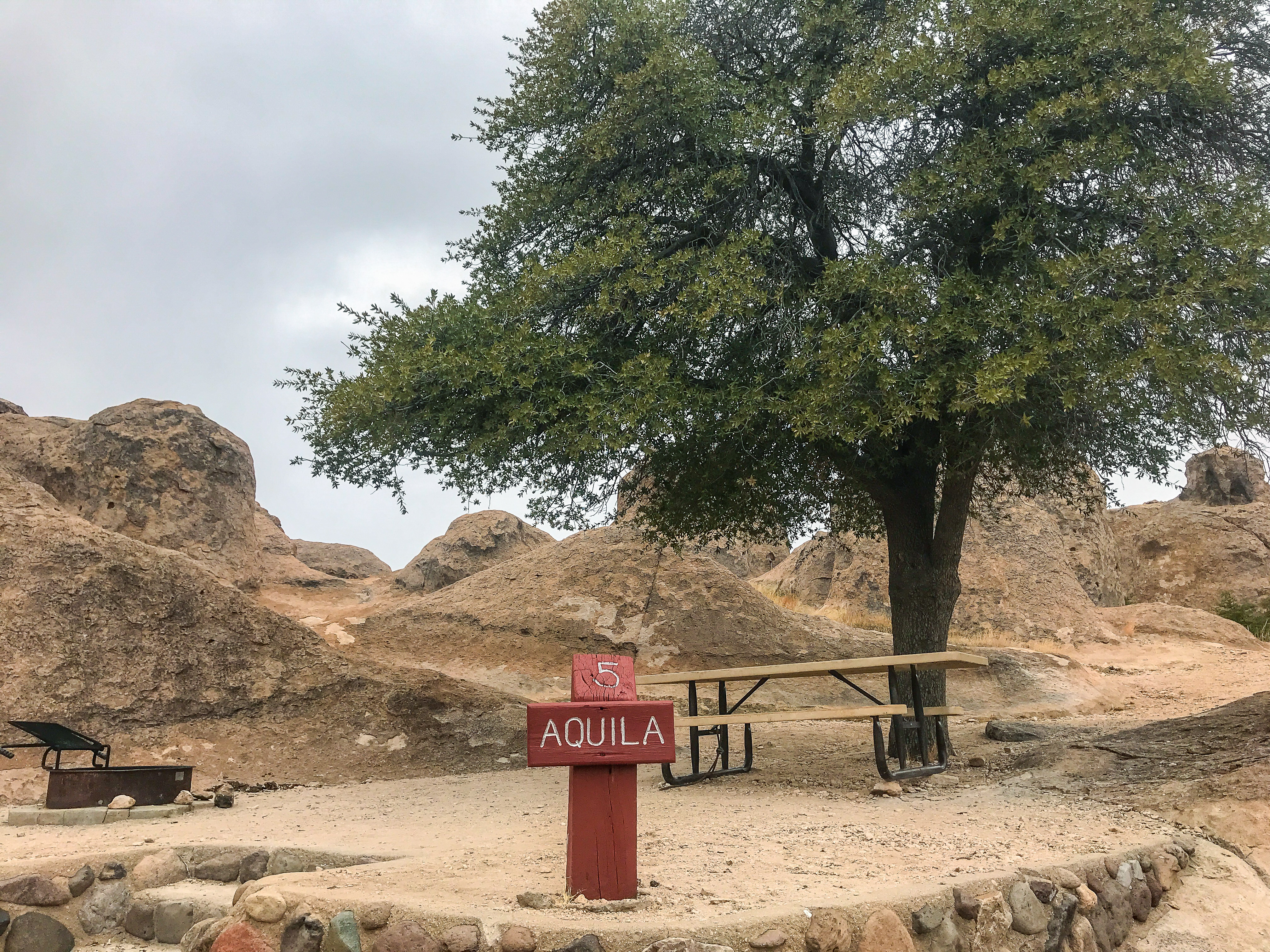 A well-maintained campsite at City of Rocks State Park featuring a picnic table, fire ring, and campsite marker #5 Aquila sign, set against the backdrop of the park's distinctive rock formations, ideal for outdoor enthusiasts