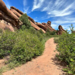 Panoramic view of the Red Rocks Trading Post Trail showcasing towering red rock formations and the trail winding through them.