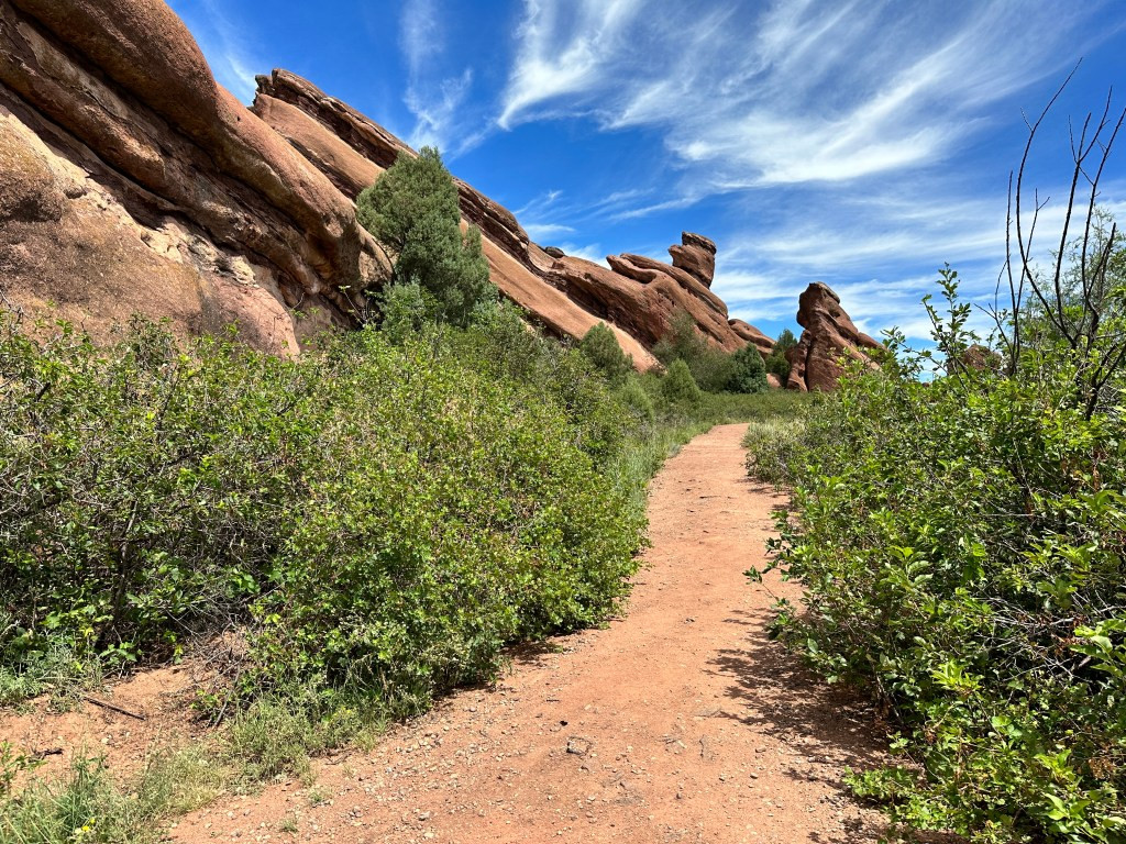 Panoramic view of the Red Rocks Trading Post Trail showcasing towering red rock formations and the trail winding through them.