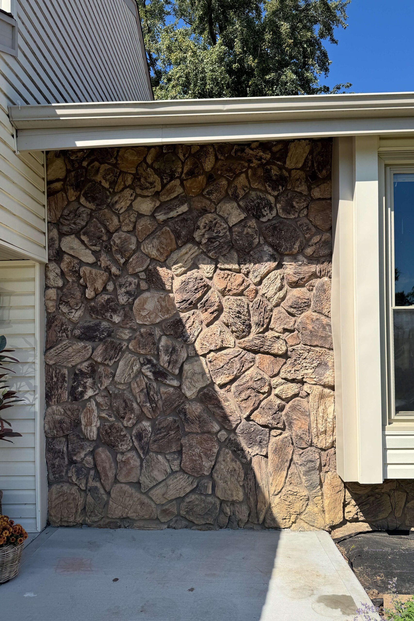 Wide before picture showing the extent of dated rock siding on the home exterior.