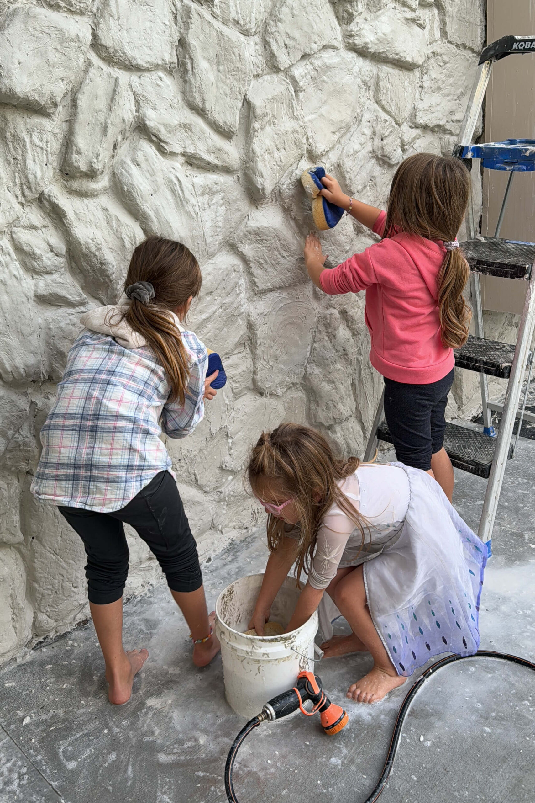 Friends using sponges to smooth the mortar on the exterior rock siding, making it a fun group activity.