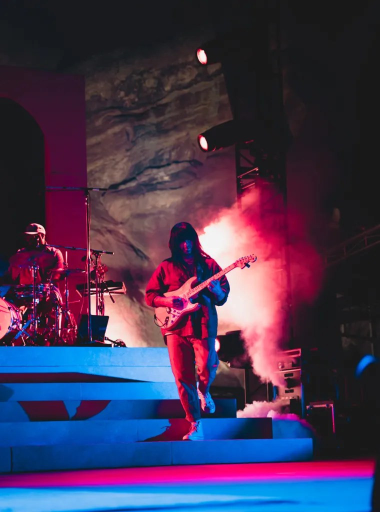 Khruangbin performing under the dramatic lighting of Red Rocks, enhancing their ethereal musical style.