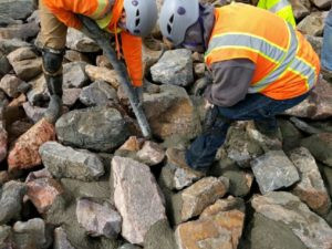 Construction workers applying grout to matrix rip rap for enhanced riverbank protection