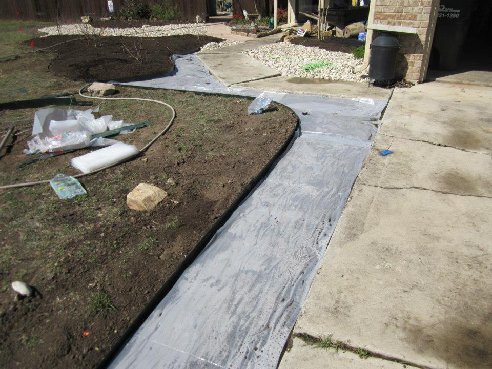 Preparing garden bed for rock installation by laying down plastic sheeting after soil removal.