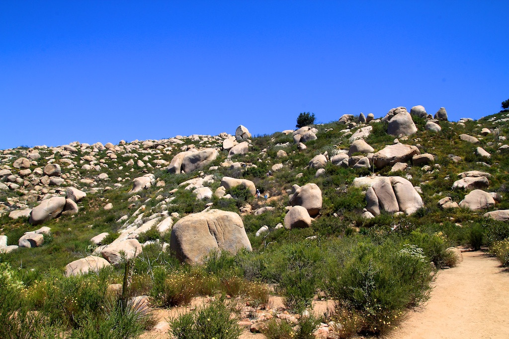 Panoramic view from the Potato Chip Rock trail, showcasing distant mountains and urban sprawl as hikers ascend towards the iconic rock formation.