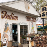 Rainbow Rock Shop in Holbrook, Arizona, featuring large dinosaur statues, signage, and a building, under a bright sky