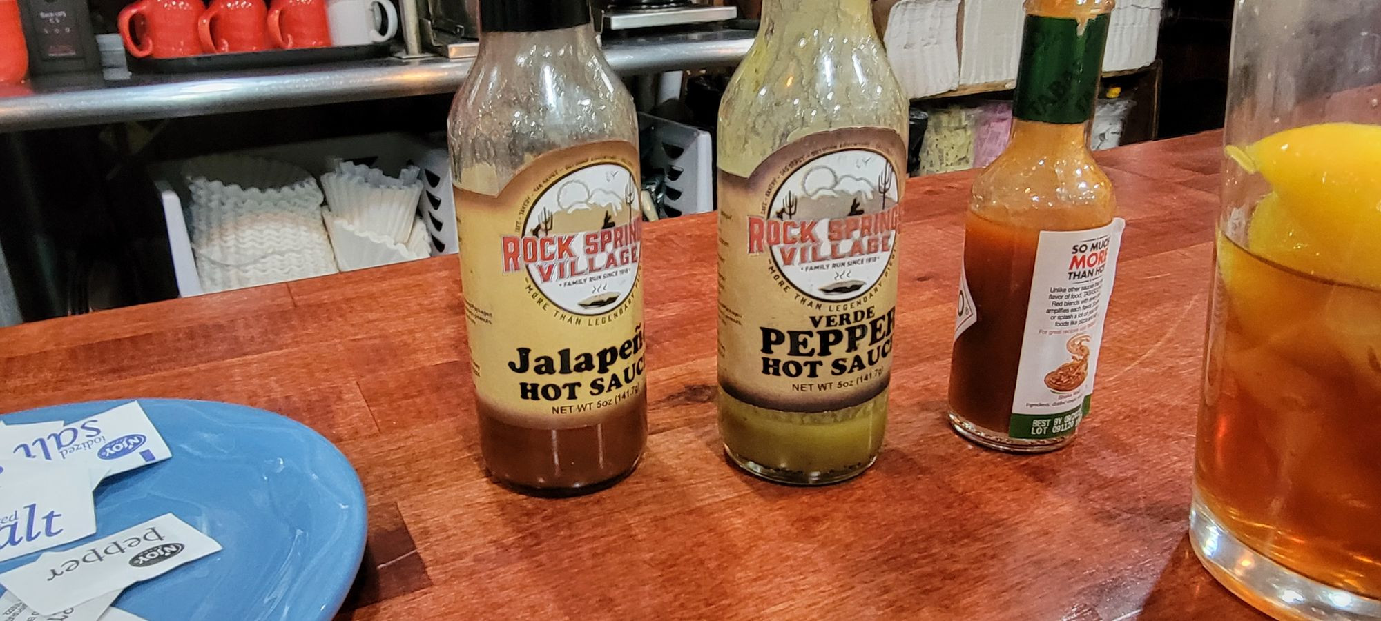 An array of custom hot sauces at Rock Springs Cafe, including Jalapeno and Verde pepper varieties, each topped with a playful cowboy hat.