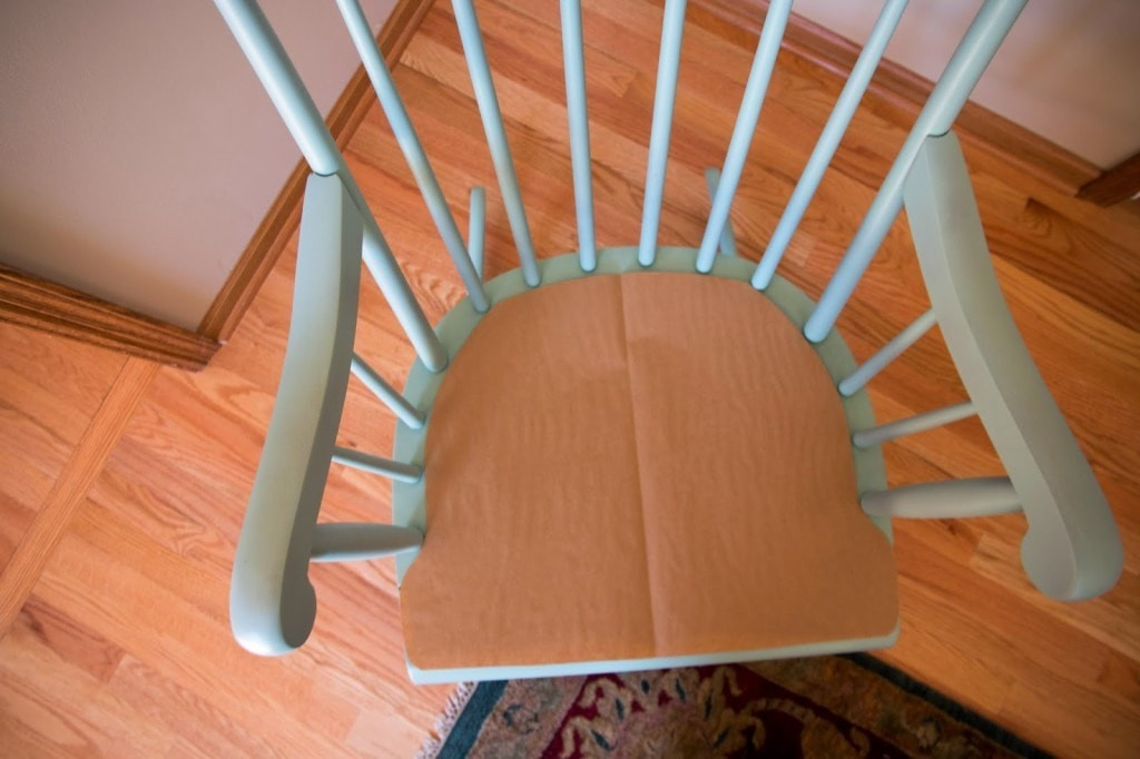 DIY process of creating a template for an upholstered rocking chair cushion, showing paper and marker