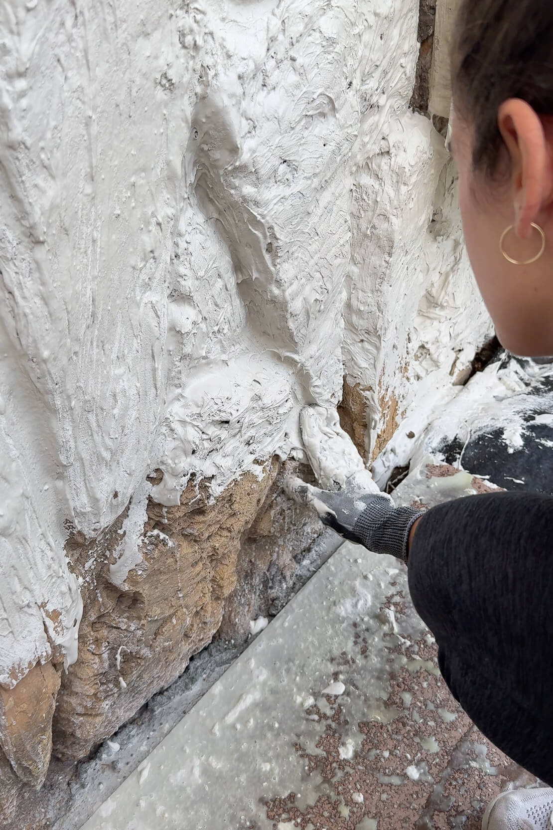 Applying mortar to a section of dated rock siding on a home exterior.