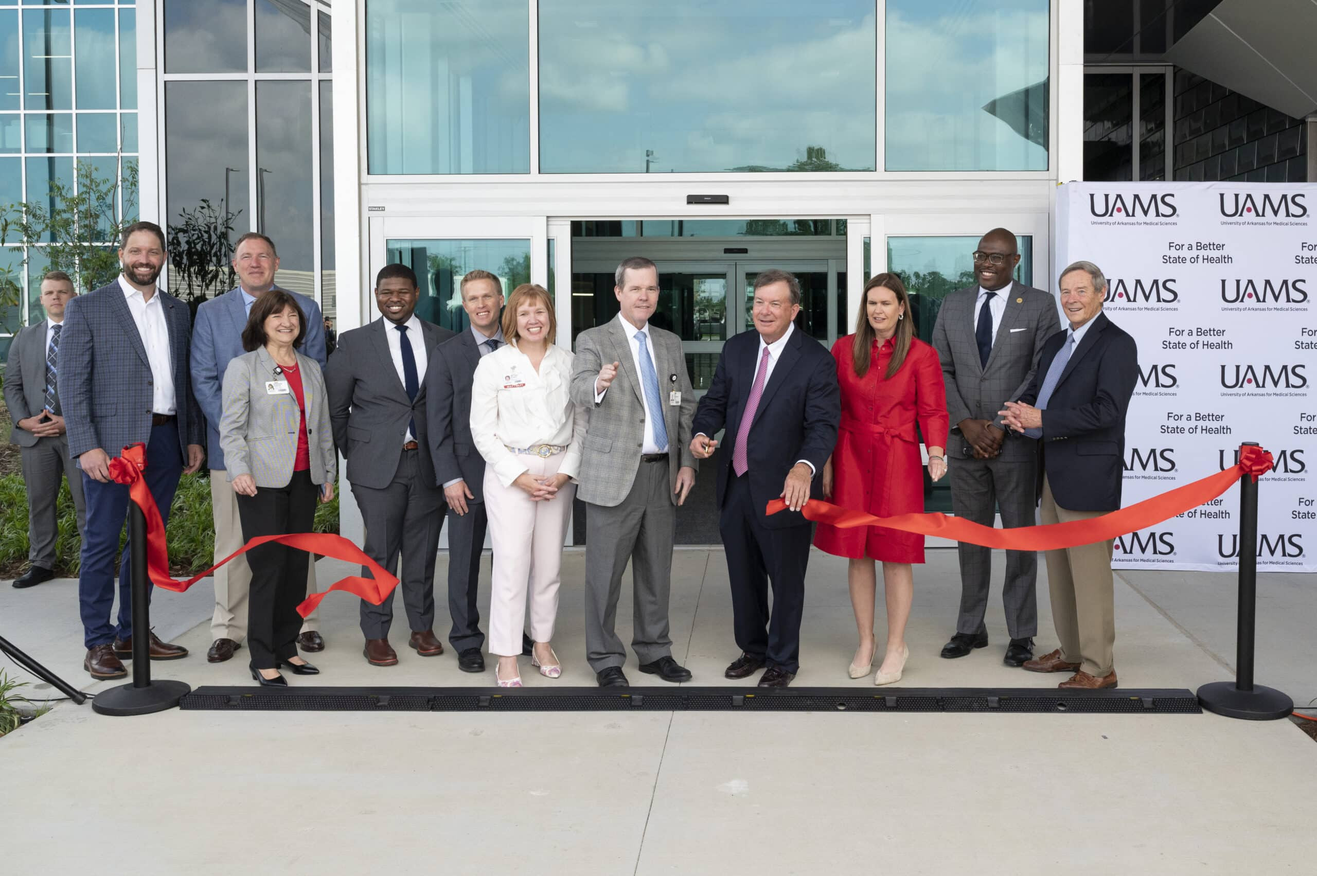 UAMS Chancellor Cam Patterson, Gov. Sarah Huckabee Sanders, and Dr. C. Lowry Barnes cut the ribbon at the Orthopaedic & Spine Hospital opening, surrounded by hospital and city officials.