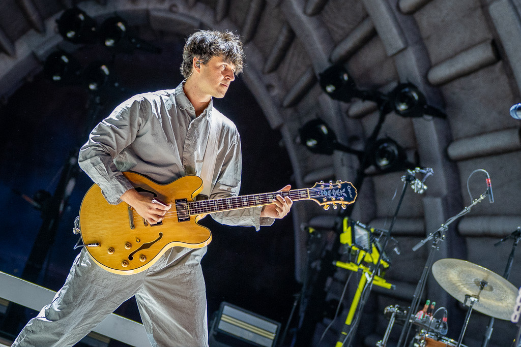 Ezra Koenig of Vampire Weekend singing and playing guitar at Red Rocks Amphitheatre during their 2024 concert.