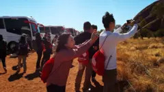 Tourists taking photos from the base walk area at Uluru, showcasing the beautiful landscape and cultural significance