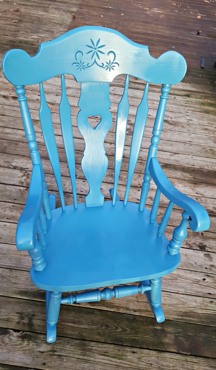 Applying spray paint to the rocking chair outdoors.