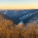 Warm sunlight on the bare branches of the trees contrasts with the cold snow-covered Cheat River gorge, showcasing the beauty of Coopers Rock in winter.