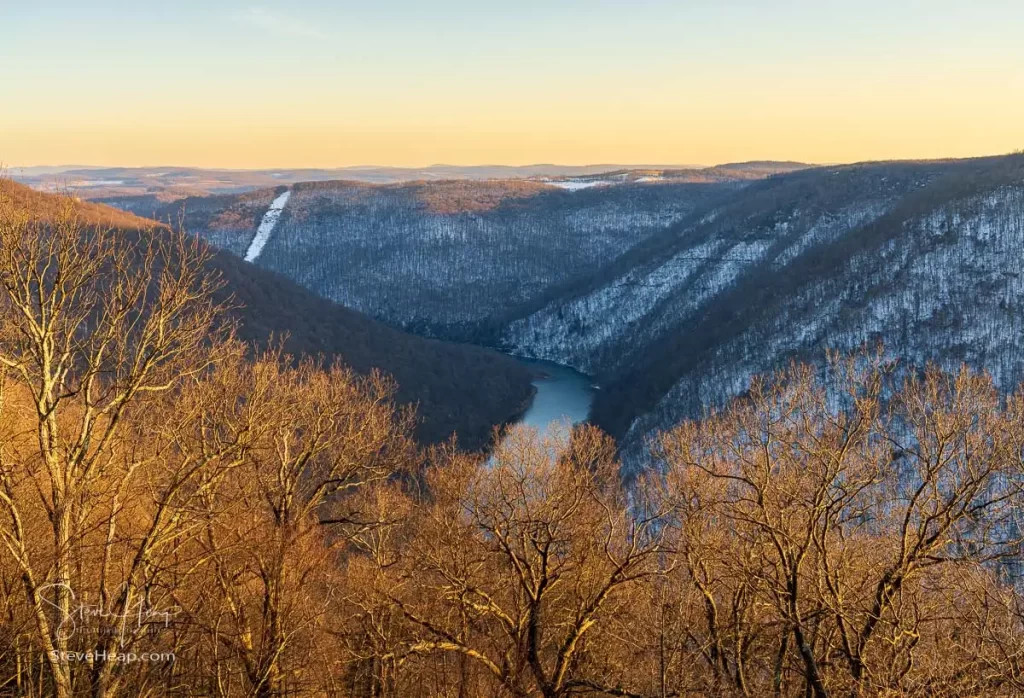 Warm sunlight on the bare branches of the trees contrasts with the cold snow-covered Cheat River gorge, showcasing the beauty of Coopers Rock in winter.
