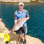 Angler casting lure from rocky shoreline with crashing waves