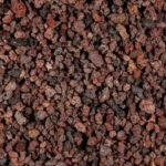 Red lava rock used in a garden bed, providing a visually appealing contrast with green plants