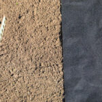 A piece of nonwoven landscape fabric sits on a prepared bed of soil where a garden rake rests