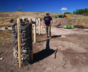 Backfilling the base of a rock fence post to add extra support, demonstrating the layered construction technique
