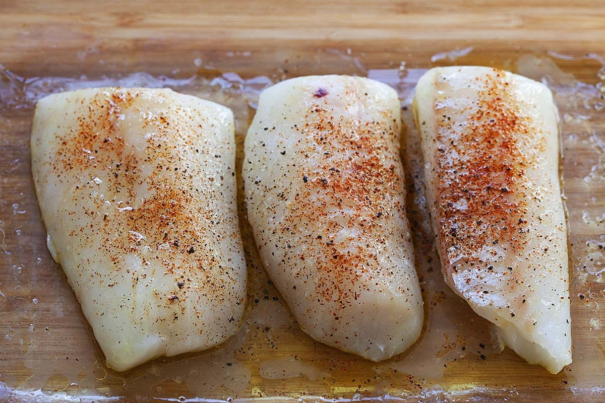 Seasoned rock cod fillets ready for the oven, showcasing fresh herbs and lemon slices for added flavor.