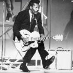 Chuck Berry playing guitar doing his famous duck walk, his style of play is studied by rock and roll guitarist to this day