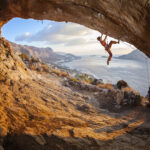 Rock climber ascending a challenging rock face with blue sky in the background