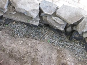 Drainage system behind rock wall with gravel and landscape fabric