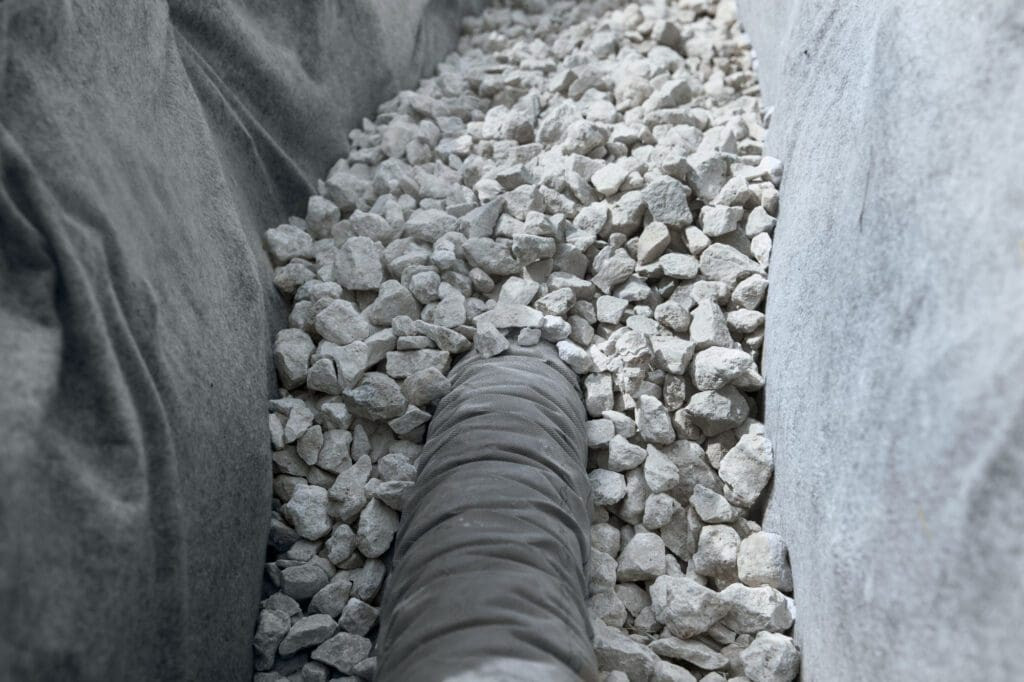 Nonwoven landscape fabric surrounding a French drain, separating rock from soil