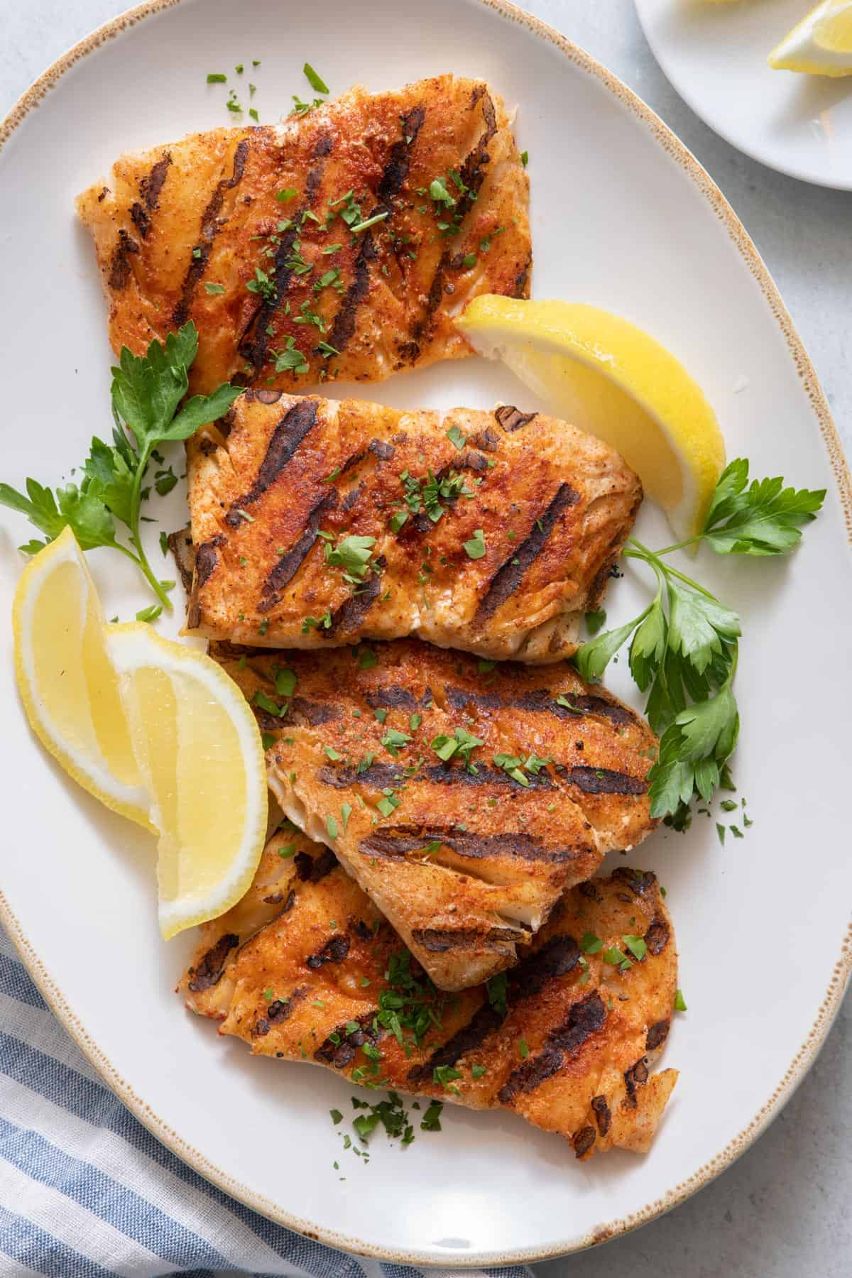 Plater of 4 grilled cod filets garnished with lemon wedges and chopped parsley