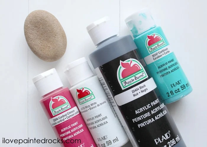 Supplies for painting a ladybug rock, including acrylic paints, paintbrushes, and smooth rocks