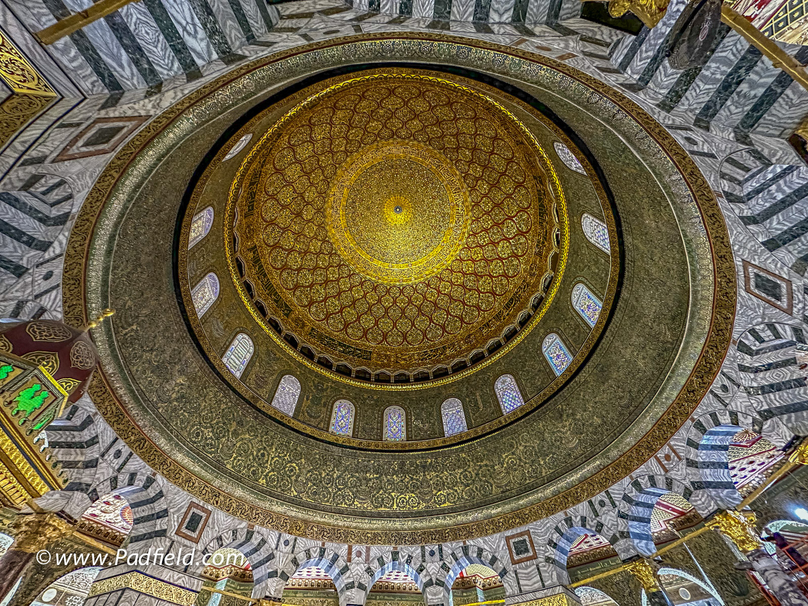View looking up at the interior of the Dome, highlighting the Arabic inscriptions and mosaic patterns.