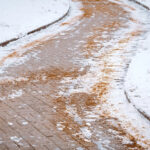 Rock salt being spread on a snowy driveway for de-icing, ensuring safe passage during winter.