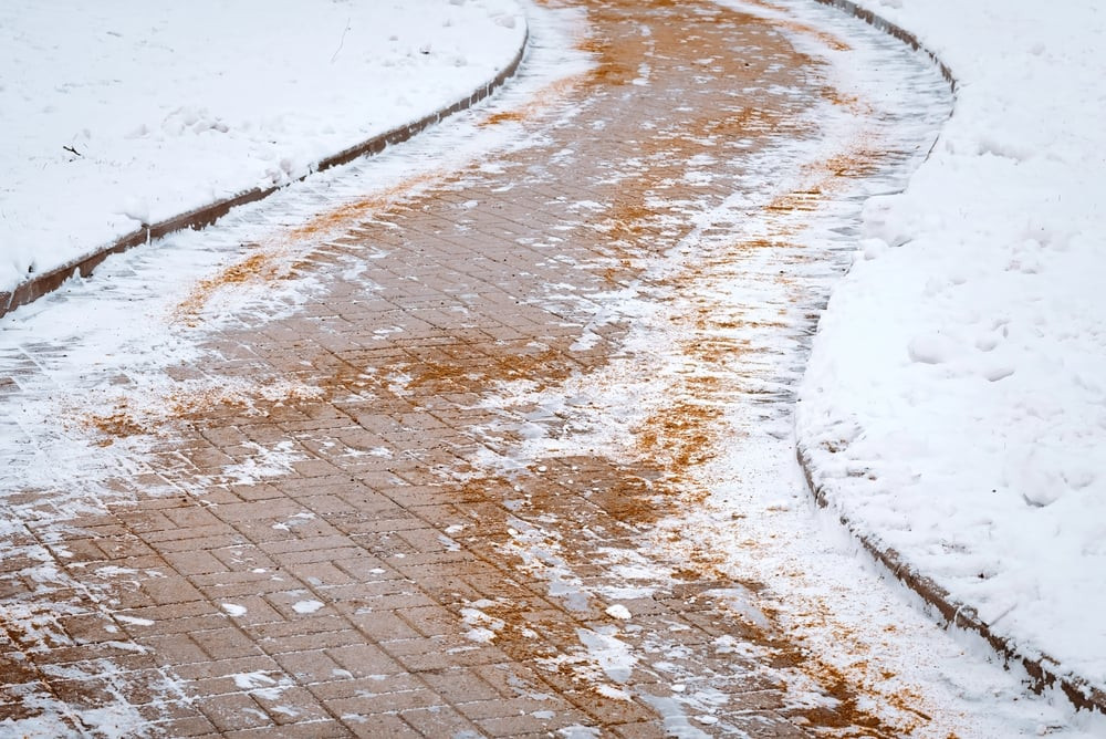 Rock salt being spread on a snowy driveway for de-icing, ensuring safe passage during winter.