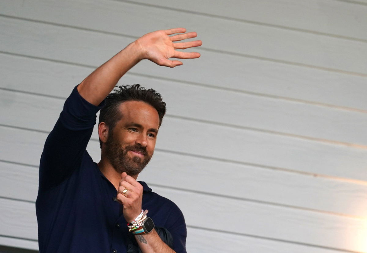 Ryan Reynolds waves in the stands during a Wrexham match, showcasing his engaging public persona and entrepreneurial spirit.