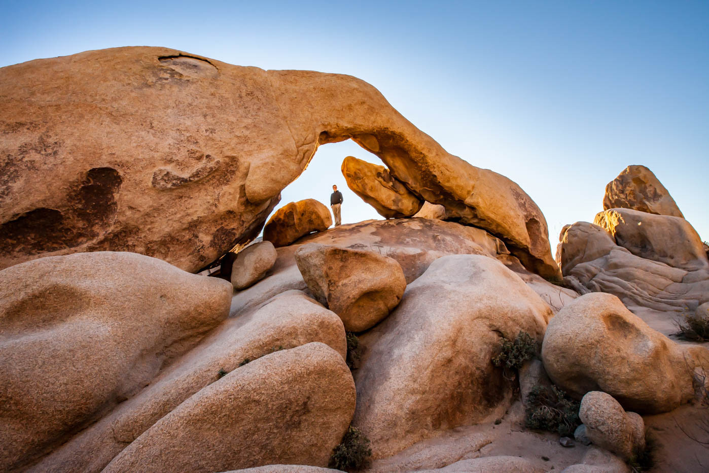 A person walking under Arch Rock at Joshua Tree National Park