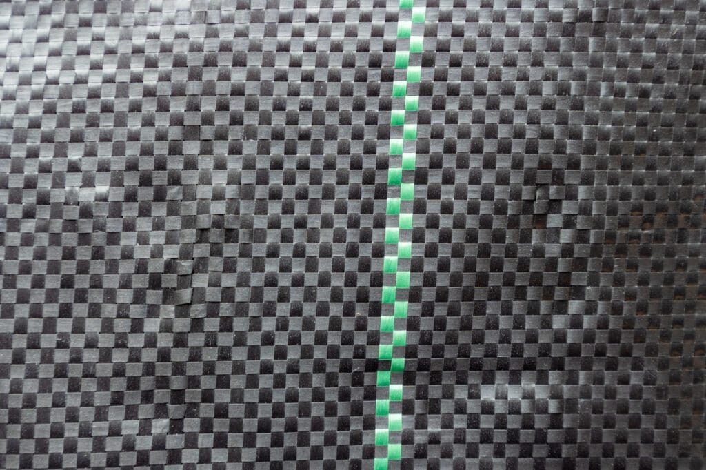 Closeup of woven landscape fabric showing its crisscross threads and green alignment line