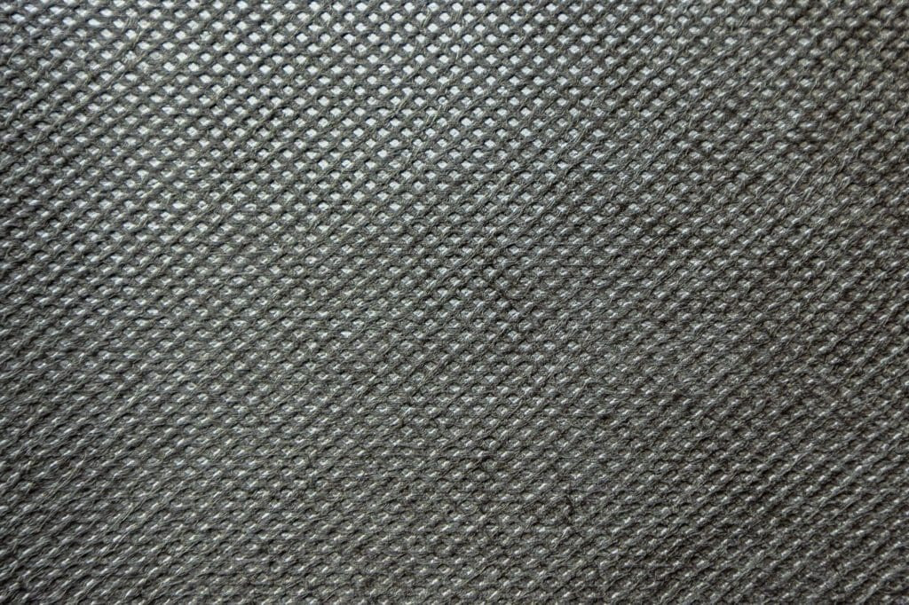 This close-up of point bond fabric reveals a repeating diamond pattern, heat-sealed to maintain permeability and bonding strength for effective weed control and soil stabilization.