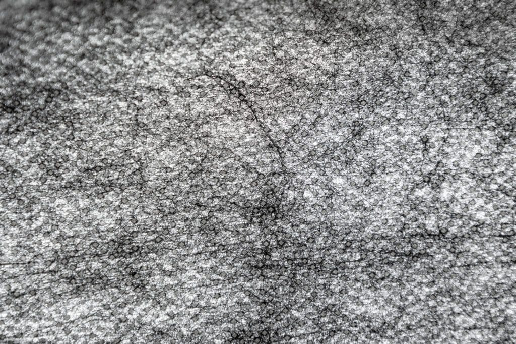 This close-up of point bond fabric, illuminated by a light source, highlights the pattern of sealed dots that enhance its strength and permeability for effective landscape use.