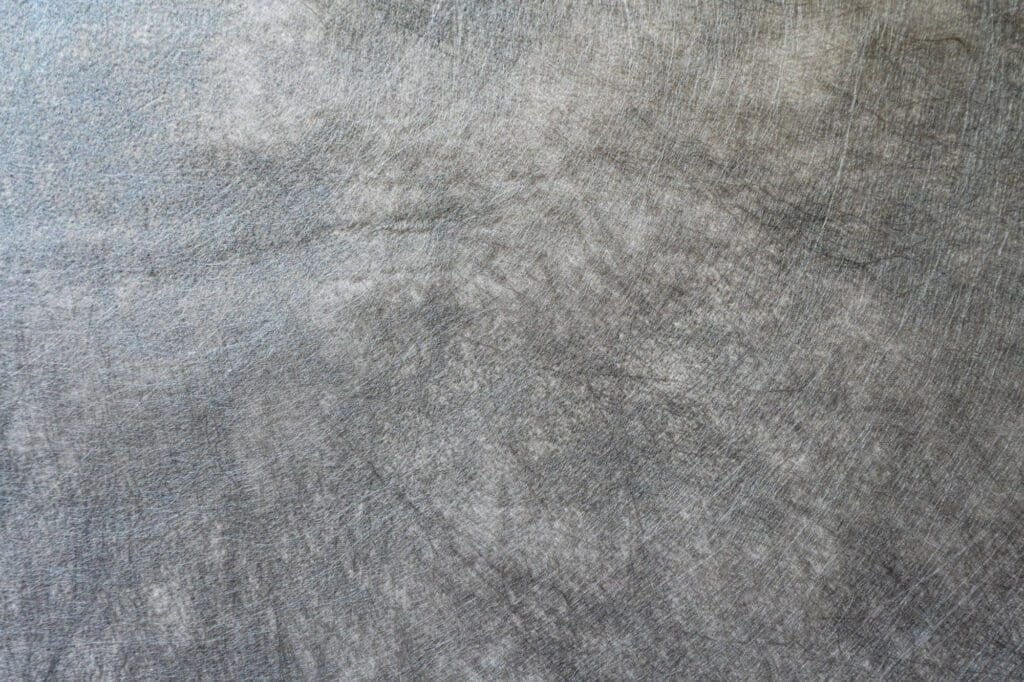A close-up of gray nonwoven landscape fabric shows the random intersection of fibers, providing permeability for effective drainage in various landscaping applications.