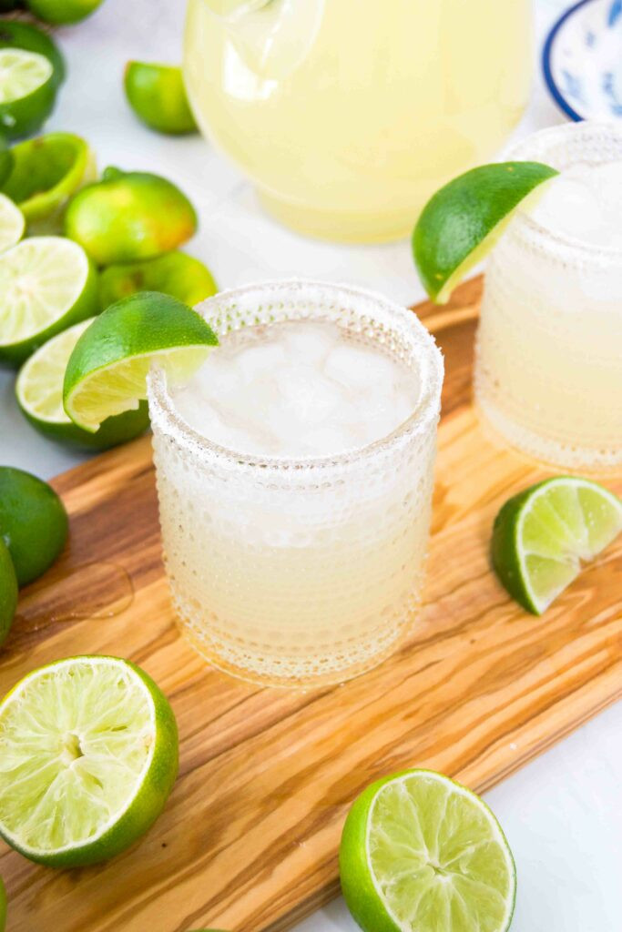 Two margaritas with limes and salt on a cutting board